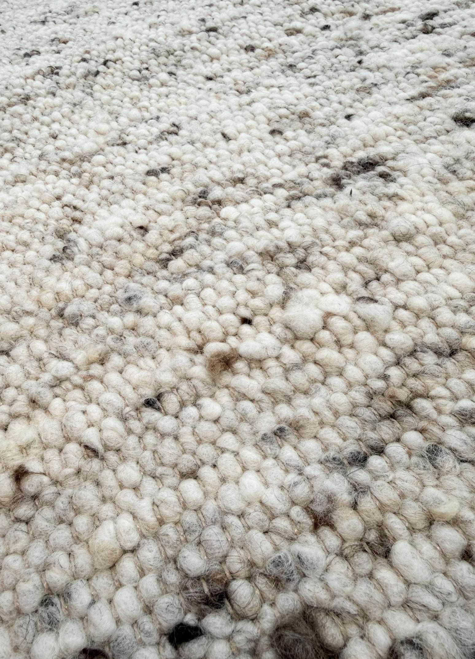 Mellow Sand kilimas iš arti, kur matoma jo tekstūra su smulkiais vilnos rutuliukais ir smėline, pilka, juoda spalva ir šviesiai rudais siūlais.