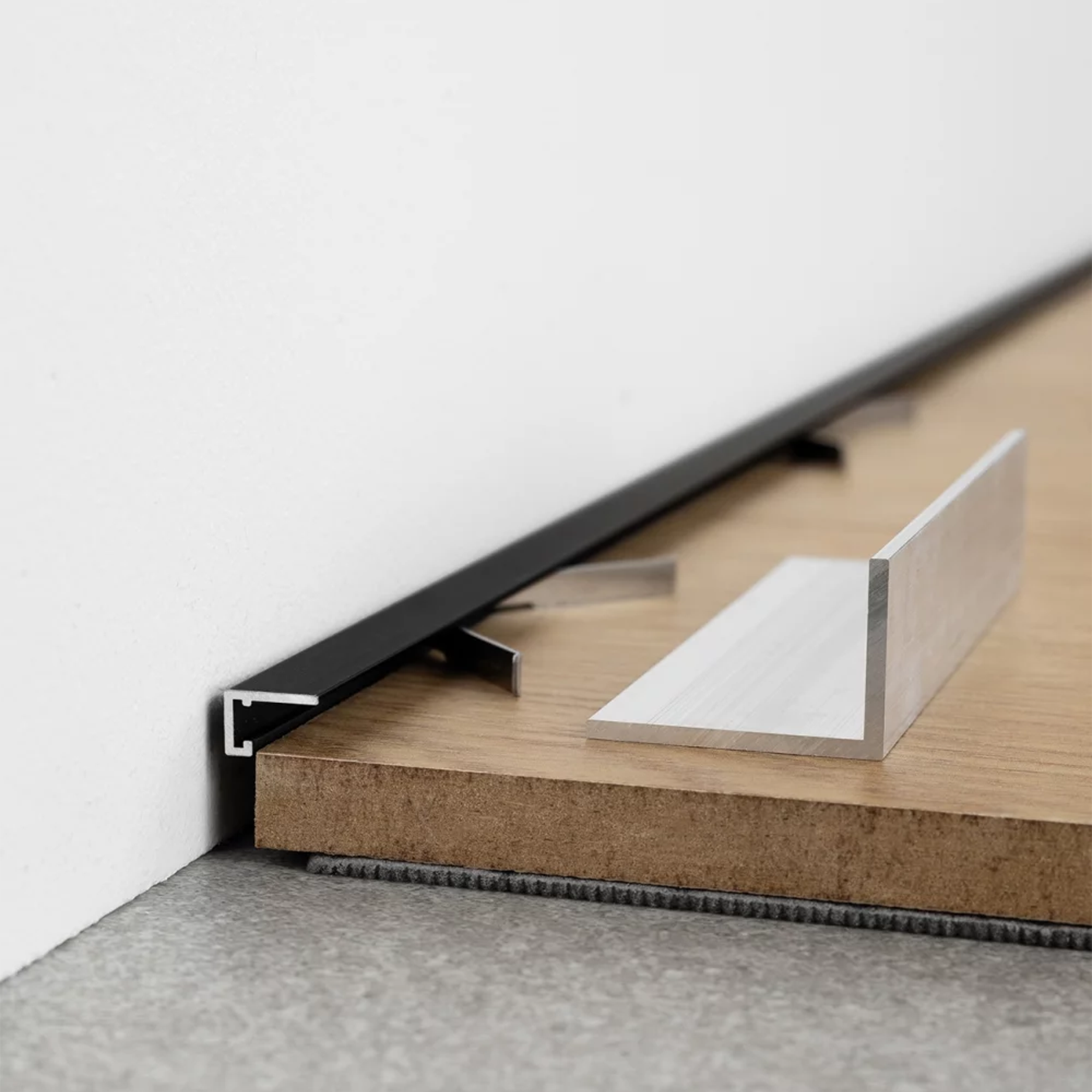 Juodos spalvos minimalistinė grindjuostė šalia baltos sienos