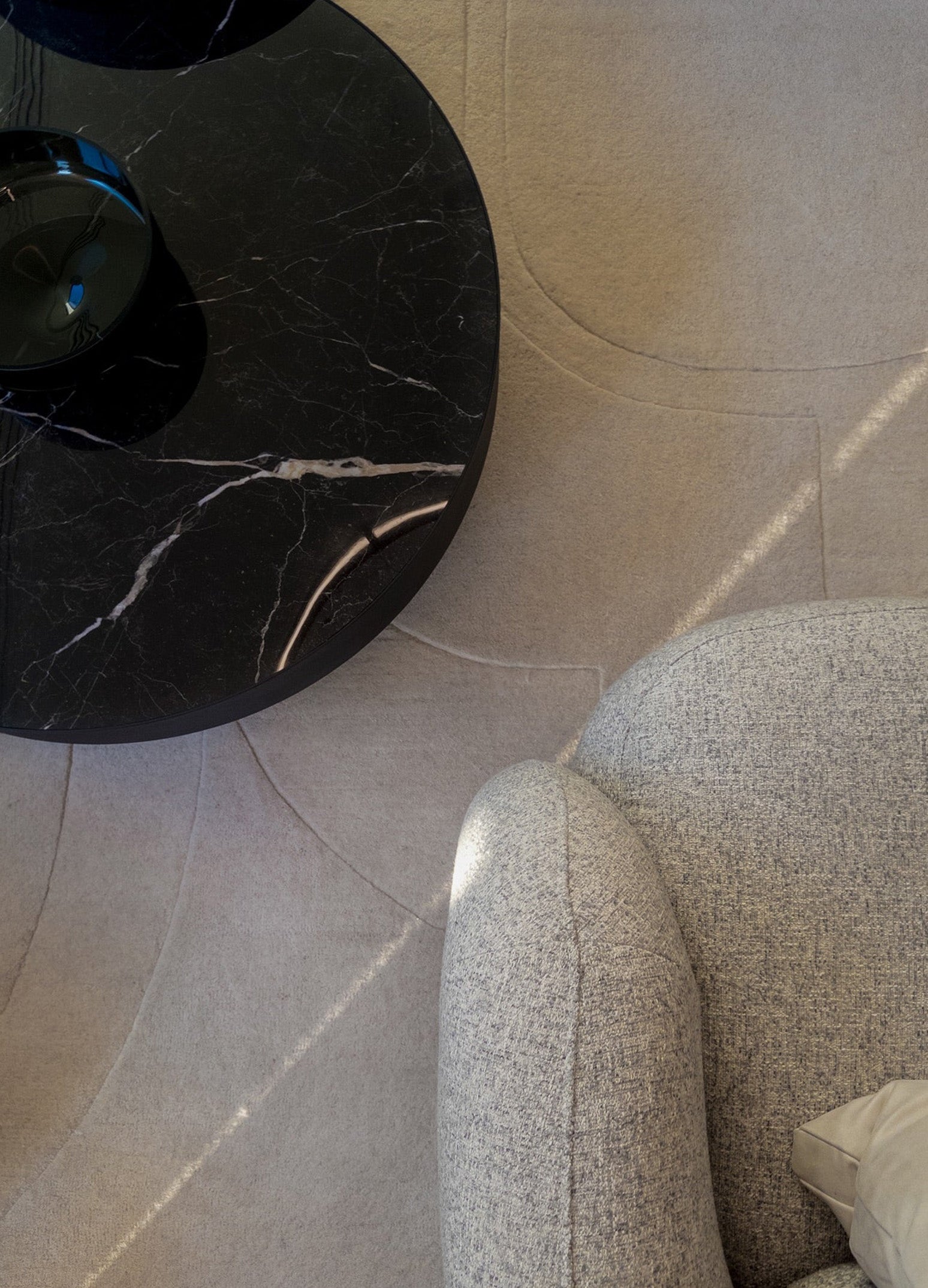 Natūralios smėlinės spalvos vilnos kilimas šalia fotelio ir juodo marmuro kavos staliuko. Makeyourcasa.lt